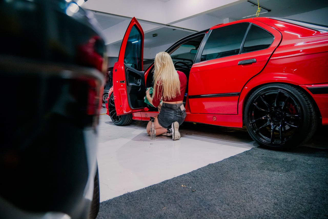 hero-img-02 A woman kneels, cleaning the interior of a red BMW in a garage environment.